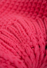 Knitted throw blanket in bright pink; features a textured pattern with raised, interwoven strands for a cozy appearance.