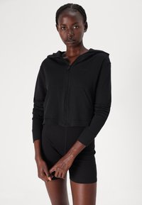 Svart kort hoodie i mjukt tyg med dragkedja fram och två fickor. Har en huva och Calvin Klein-logotyp på bröstet.