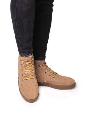 Scarpe alte marroni con una trama a spina di pesce, dotate di lacci gialli e occhielli neri, abbinate a jeans scuri.
