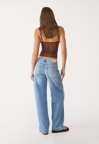 Brauner, taillierter Tank-Top, kombiniert mit hellblauen, lockeren Jeans, die zwei Gesäßtaschen und ein beiges Etikett am Bund haben.