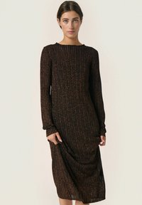 Robe noire longue avec texture côtelée, ornée de taches orange. Encolure dégagée et manches longues, atteignant le molet avec une coupe ample.