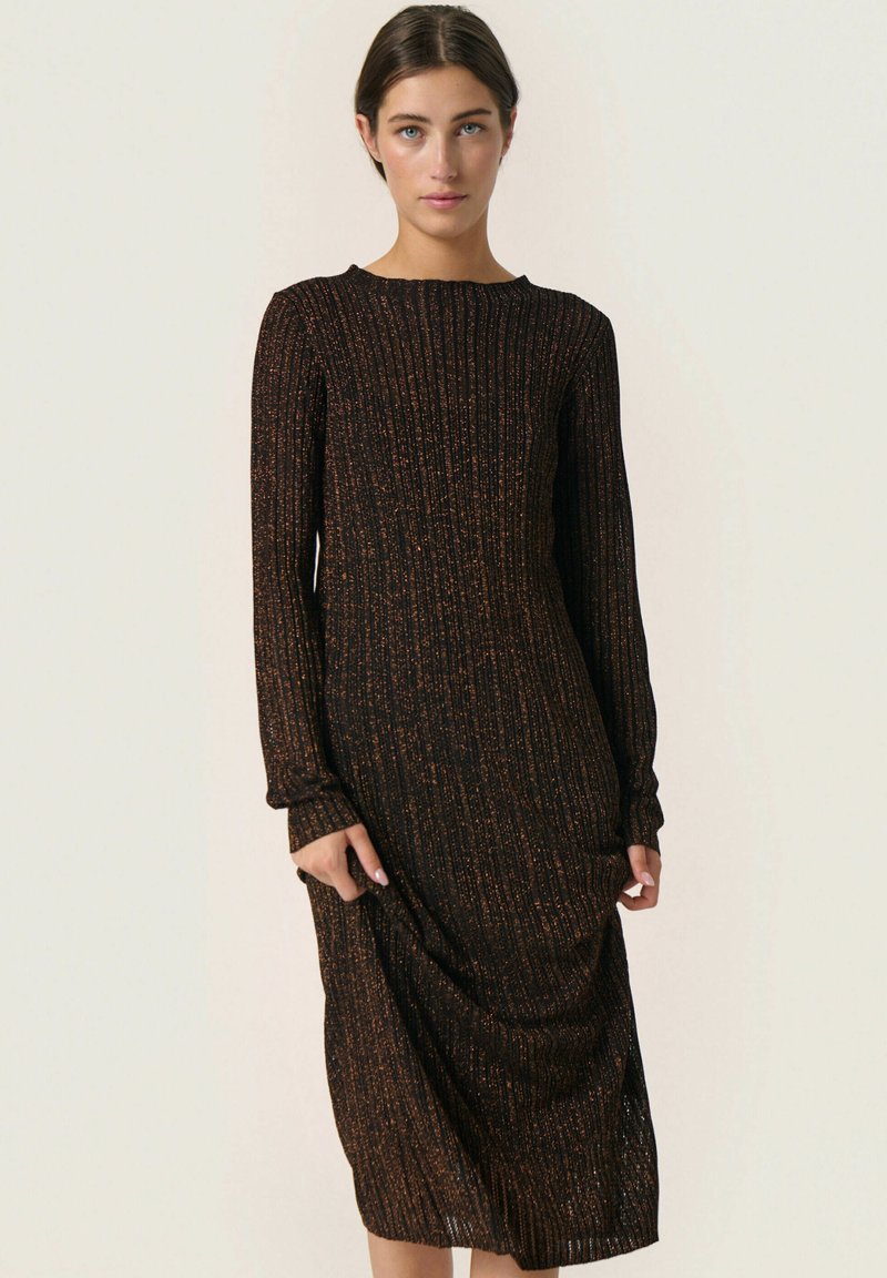 Robe noire longue avec texture côtelée, ornée de taches orange. Encolure dégagée et manches longues, atteignant le molet avec une coupe ample.