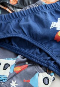 Sous-vêtements pour enfants empilés avec des motifs sur le thème de l'espace, incluant des fusées et des étoiles, en couleurs bleue et grise.