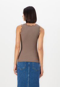 Débardeur marron à côtes avec un bord en dentelle sur les épaules, assorti d'une jupe en denim mi-longue avec des poches arrière et un détail de couture.