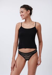 Zwarte cropped tanktop met dunne bandjes, gecombineerd met een zwarte kanten string met bloemenpatronen en geschulpte randen. Gladde stoftextuur.