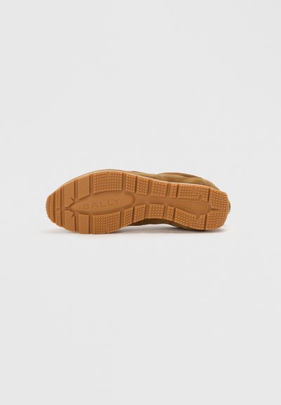 Zapatilla de ante marrón con una suela de goma texturizada, que presenta un agarre con patrón y un logo en relieve. Forma redondeada con costuras reforzadas.
