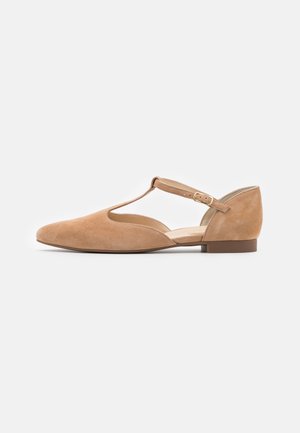 Chaussure plate en daim beige avec bride en T et fermeture à boucle, petit talon et bout pointu, présentée sur un fond clair uni.