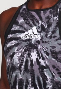 Bezrekawnikowa czarno-szara sportowa koszulka z graficznym wzorem i białym logo Adidas; posiada gładką fakturę i okrągły dekolt.