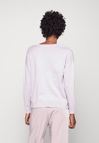 Light lavender sweater with a relaxed fit, ribbed cuffs and hem, soft texture, and dropped shoulders, paired with light beige pants.