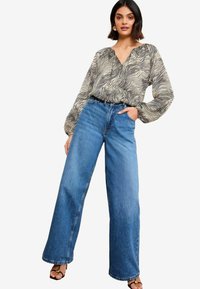 Black and white zebra-patterned blouse with a V-neck, paired with high-waisted, wide-leg blue denim jeans. Sandals with a gold accent.