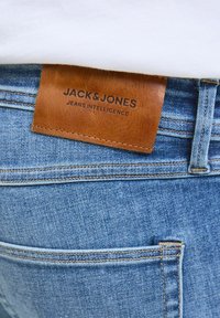 Modra kavbojka z označbo iz svetlo rjave teksturirane usnje z črnim napisom "JACK & JONES" in "JEANS INTELLIGENCE."