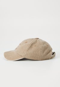 Beige baseball cap with a textured fabric, curved brim, five ventilation holes, and an adjustable strap at the back.