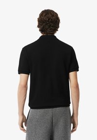Czarny t-shirt polo o miękkiej fakturze, z krótkimi rękawami i klasycznym kołnierzykiem. Charakteryzuje się czystym, prostym designem bez widocznych logo.