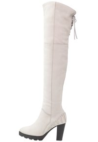 Wysoka, kremowa skórzana botka na obcasie z masywną czarną podeszwą, bocznym przeszyciem oraz sznurowaniem z tyłu w okolicy górnej części.