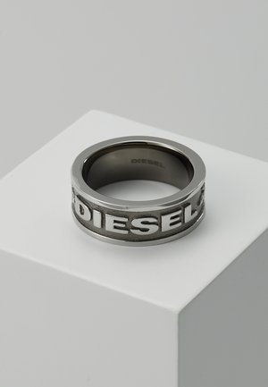 Anillo de metal con un acabado negro mate y letras en relieve "DIESEL" alrededor de la banda. Superficie exterior lisa, interior redondeado.