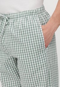 Pantalons à carreaux verts et blancs avec taille élastique, cordon ajustable et poches latérales. Fabriqués dans un tissu léger.