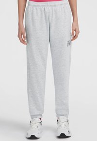 Persoon in lichtgrijze sweatpants met elastische taille en boorden, klein hartjeslogo op de dij en witte sportschoenen.