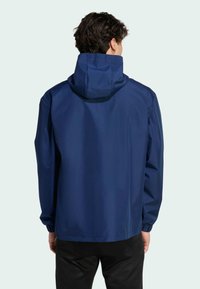 Ναυτικό μπλε αδιάβροχο μπουφάν με κουκούλα, ελαστικούς καρπούς και ευθεία γραμμή. Λείος υφασμάτινος ιστός, μινιμαλιστικός σχεδιασμός, χωρίς ορατά σχέδια.