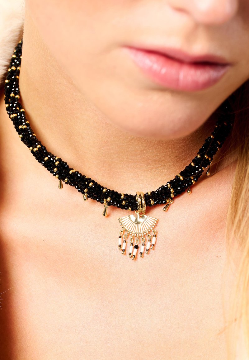 Collier ras de cou noir orné de perles dorées, avec un pendentif en forme d'éventail et des perles pendantes, placé de manière proéminente autour du cou.