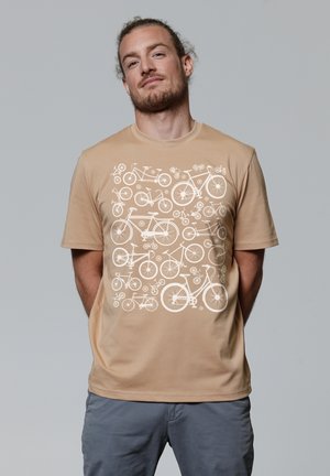 Beige katoenen T-shirt met een wit fietsontwerp aan de voorkant. Ronde hals met korte mouwen en een losse pasvorm.