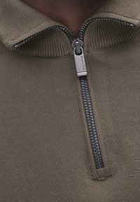 Olivengrüner Reißverschluss-Pullover mit Rippstruktur, der einen silbernen Reißverschluss und ein Stehkragen-Design aufweist.