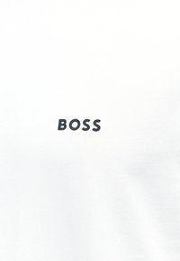 Λευκό ύφασμα με την λέξη «BOSS» τυπωμένη με μαύρα, έντονα κεφαλαία γράμματα στο κέντρο της εικόνας.