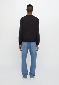 Black crewneck sweatshirt, relaxed fit, paired with light blue loose-fitting jeans and white sneakers. Smooth texture, minimal branding.