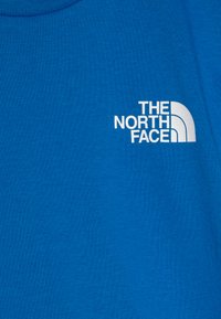 Mėlynas medvilninis marškinėliai su apvaliu kaklu. Kairėje krūtinės pusėje yra baltas "THE NORTH FACE" logotipas su kreivu grafiniu elementu.