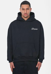Zwarte hoodie van textiel, met een voorzak en een witte geborduurde logo op de borst. Wijdere mouwen en zoom.