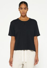 T-shirt nera a maniche corte in materiale morbido, con scollatura rotonda e un discreto dettaglio del logo sul davanti. Design dalla vestibilità rilassata.