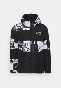 Fodrad jacka i svart och vitt, med en blandning av grafiska mönster och logotyper. Inkluderar huva och dragkedja fram. Slät textur.