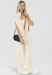 Tuta crema con gambe ampie, scialle rosa chiaro a coste e borsa a tracolla nera. Sneaker bianche completano l'outfit, con texture lisce e morbide.