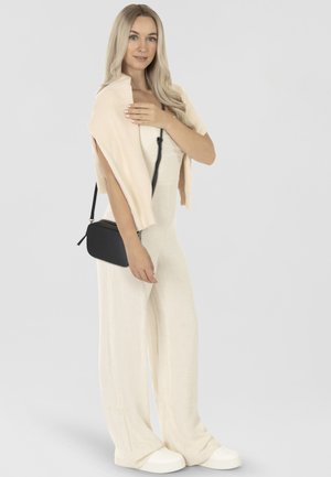 Crème jumpsuit met wijde benen, geribbelde lichtroze sjaal en zwarte crossbody tas. Witte sneakers maken de outfit compleet, met zachte, gladde texturen.