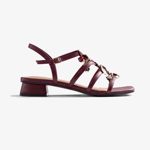 Sandale bordeaux à talon bas avec plusieurs lanières, charms décoratifs dorés et bordeaux, et une boucle réglable à la cheville.