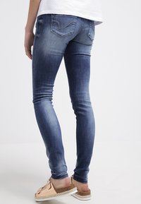 Blå denim skinny jeans har en urtvättad look, femfickorsdesign och unika bakfickor med sömdetaljer.
