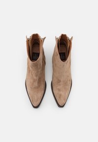 Botas de tobillo de ante color tan con puntera afilada, un interior marrón en contraste y un detalle de cremallera en la parte trasera. Superficie texturizada y diseño ajustado.