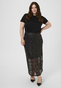 Camiseta negra combinada con una falda larga y transparente negra con patrones geométricos de lentejuelas y una silueta ajustada. Zapatos negros de punta completan el look.