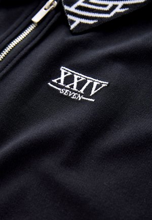 Black zip-up polo shirt with a textured fabric, featuring a white embroidered logo "XXIV SEVEN" and a patterned collar.