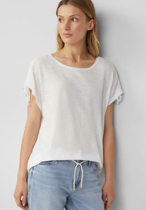 Witte top met korte mouwen en een ronde halslijn. Heeft gatherdetails bij de mouwen en een losse pasvorm. Gecodeerd met casual lichtblauwe jeans.