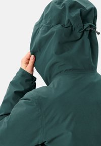 Donkergroene hoodie, gemaakt van een glad synthetisch materiaal, met een verstelbare trekkoord bij de capuchon en aansluitende manchetten. Close-up van de achterkant.