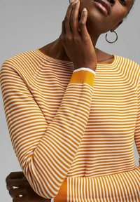 Gestreifter Pullover in Orange und Weiß, mit rundem Ausschnitt und langen Ärmeln, aus strukturiertem Strick und kontrastierenden Rippbündchen.