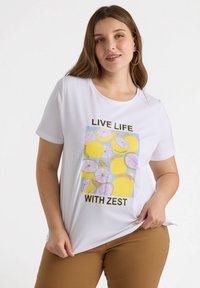 Camiseta blanca de manga corta con un colorido estampado de limones y cítricos rosas, y el texto "VIVE LA VIDA CON ENERGÍA" en negro. Textura suave.