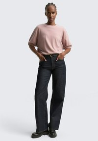 Pull oversized rose clair avec des manches courtes retroussées, associé à un jean bleu marine à jambe large et des bottes noires chunky.