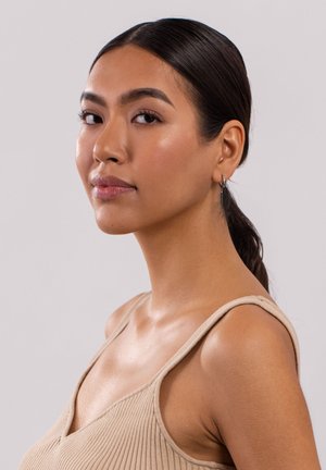 Beige ribbed tank top with thin straps. Smooth skin texture. Hair in a low ponytail. Simple hoop earring accentuates the earlobe.