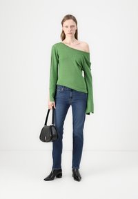 Zelena, off-the-shoulder majica z dolgimi rokavi; v kombinaciji s prilegajočimi modrimi kavbojkami in črnimi ankle čevlji s koničastim nosom; nosi črno torbico.