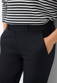 Zwarte broek van gladde stof met zijzakken, een aansluitend ontwerp en een vlakke tailleband, gecombineerd met een gestreept top.