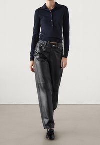 Tummansininen pitkähihaisen polo-paita nappikauluksella, yhdistettynä korkeavyötäröisiin mustiin nahkaleveälahkeisiin housuihin. Sujuva rakenne ja vartalonmyötäinen istuvuus.