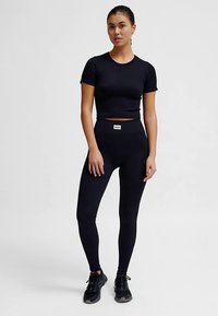 Top corto nero aderente e leggings realizzati in materiale elasticizzato. I leggings hanno una vita alta e entrambi presentano un'etichetta con il marchio sulla fascia in vita.