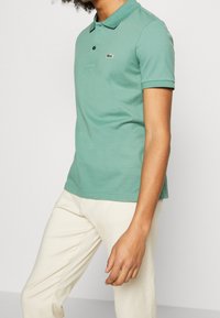 Polo en coton vert avec un col classique et des manches courtes. Présente un petit logo brodé sur la poitrine, associé à un pantalon de couleur claire.