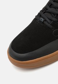 Adidași negri din suede cu talpă din cauciuc, vârf rotund și sistem de închidere cu șireturi. Prezintă un accent neted de culoare neagră și o talpă texturată de culoare bej.
